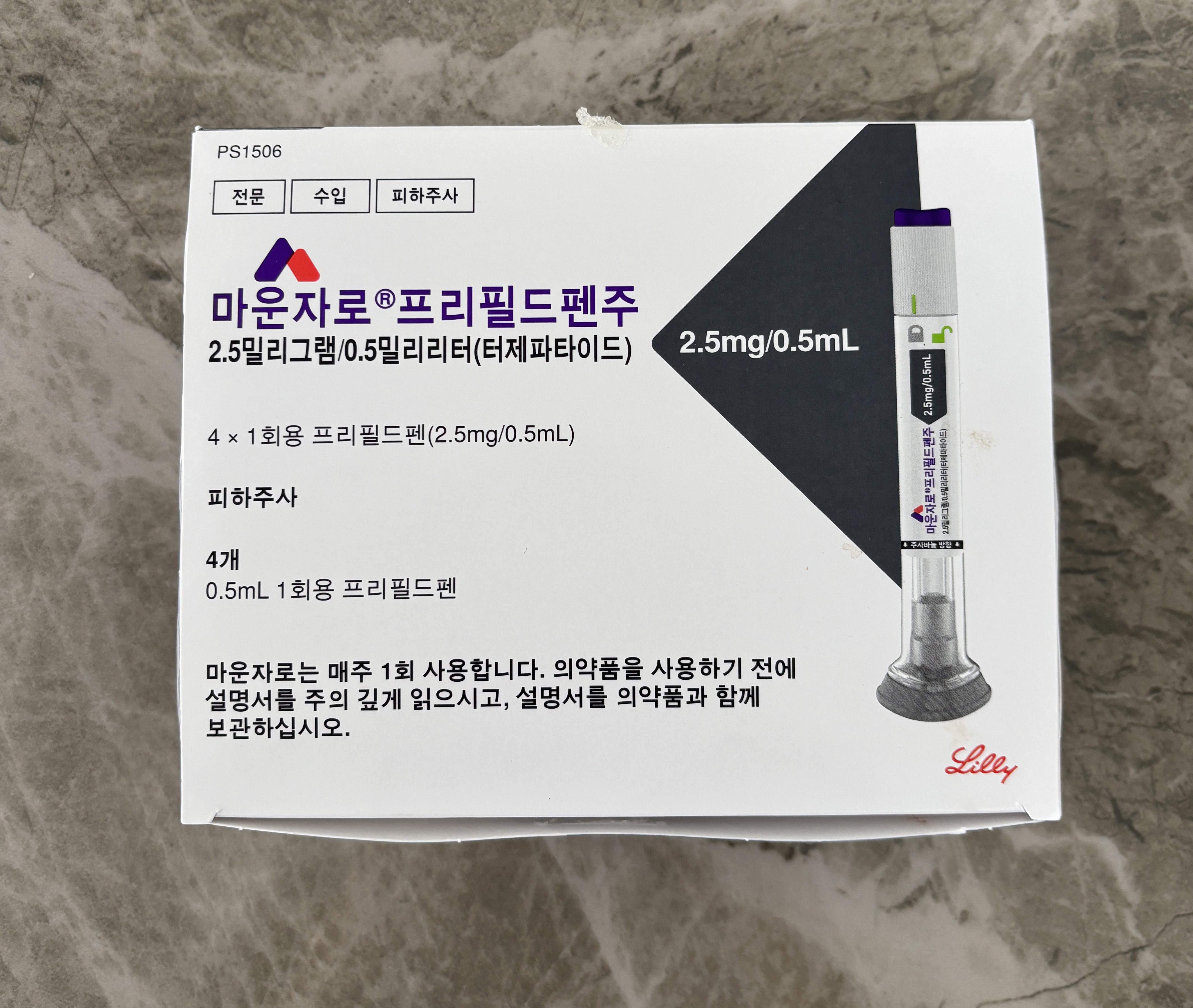 A box of medical pen injectors, labeled '마운자로' with dosage information of 2.5mg/0.5mL, containing 4 single-use pens, positioned on a gray textured surface.