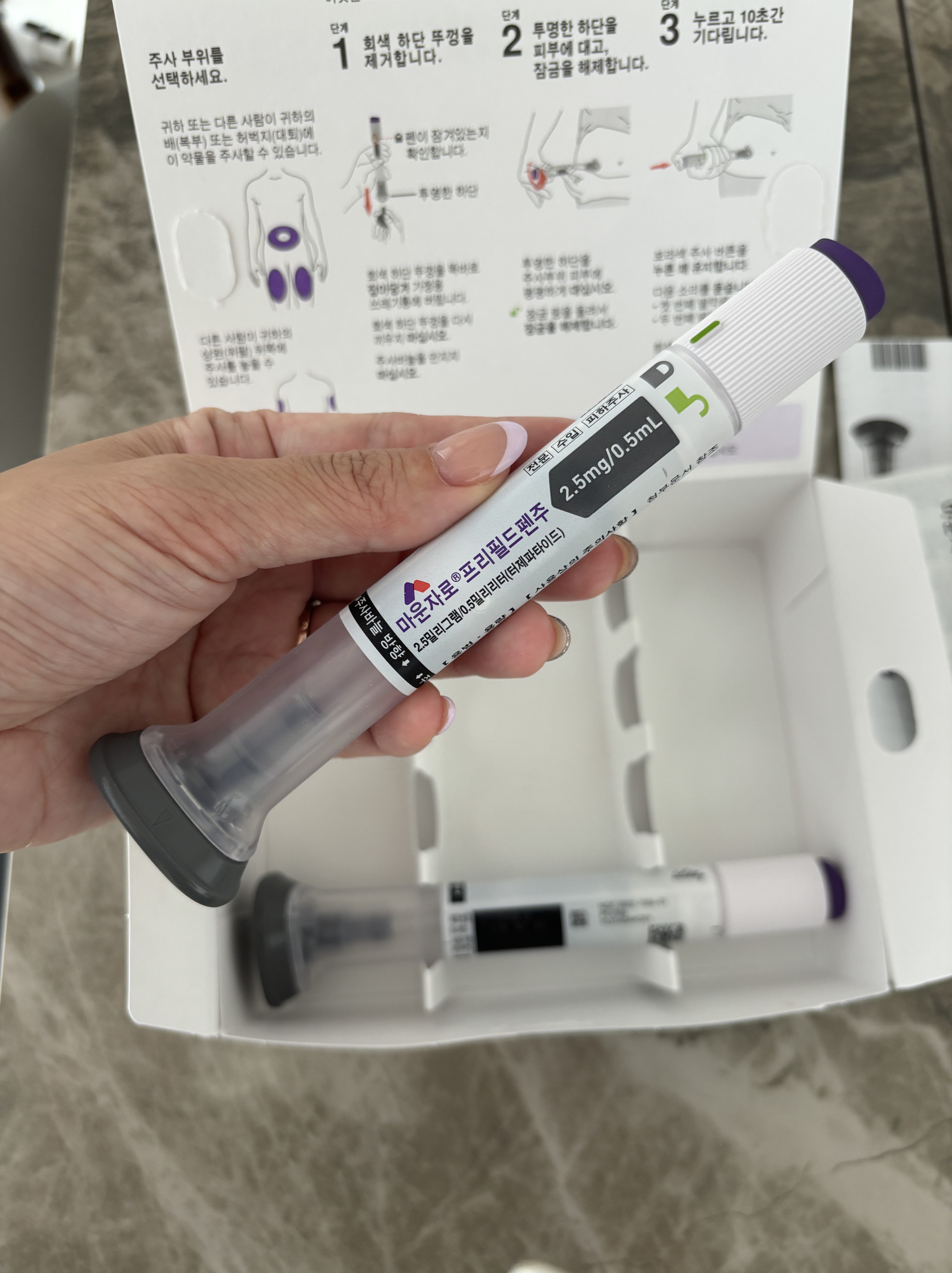A hand holding a medication delivery device with dosage details visible, set against a partially open packaging box and an informational card.