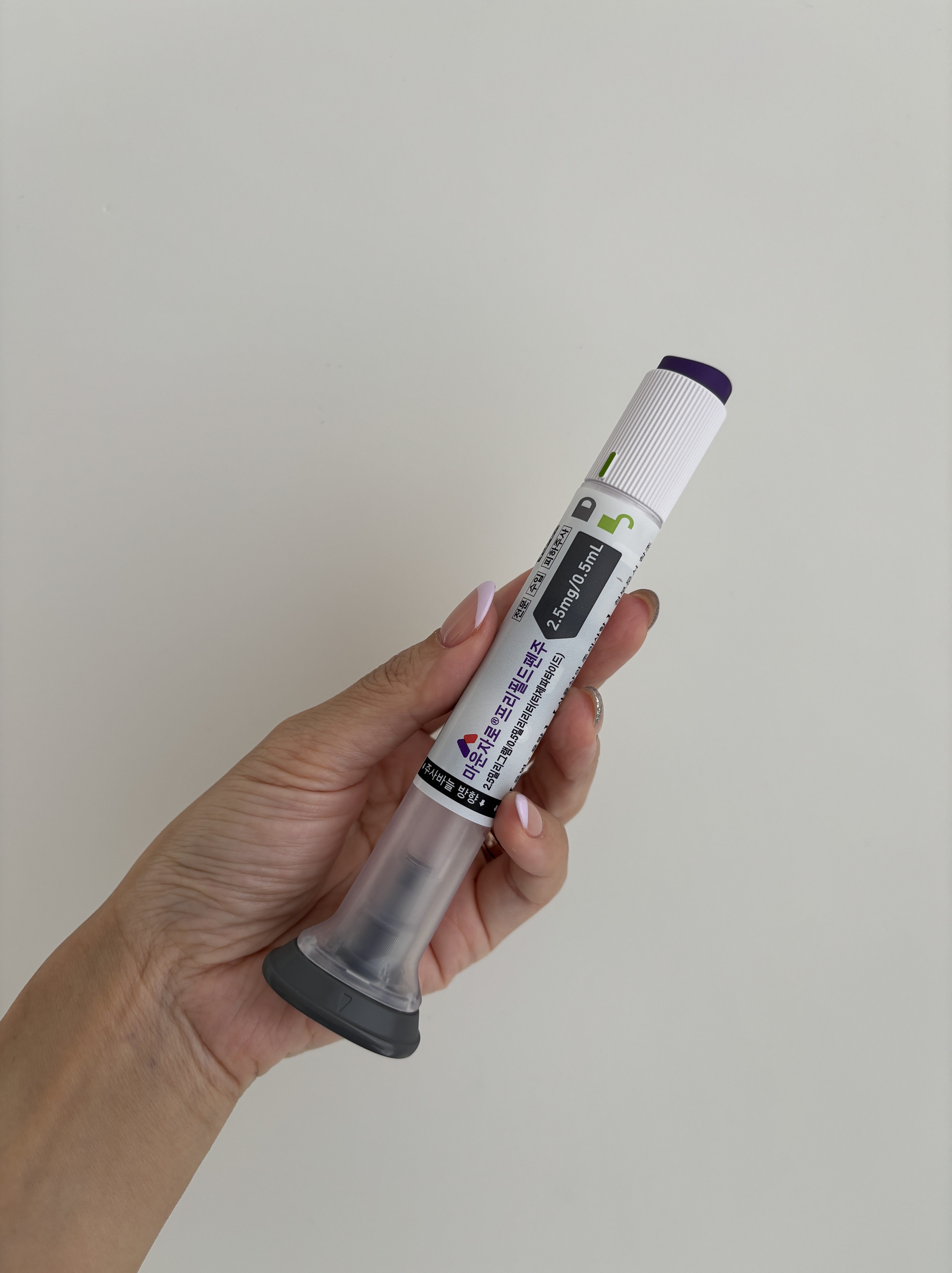 A hand holding a medication syringe with a gray tip, labeled with dosage information and designed for medical use.